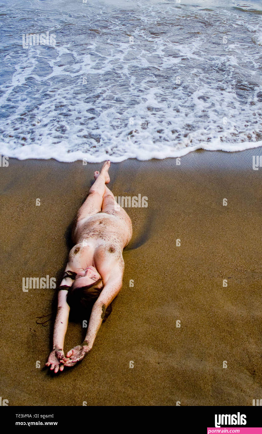 Nude sexy woman laying on Caribbean beach with waves around her and she is covered with sand Stock Photo