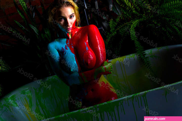 Beautiful woman with very big breasts takes a bath. Red and blue paint flows down the naked body of a girl in the bathroom. Creative body art. Stock Photo