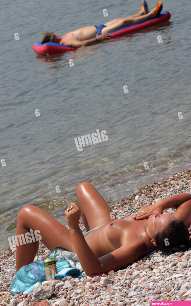 Woman sunbathing on the beach naked while a man floating on air mattress. Budva. Montenegro Stock Photo